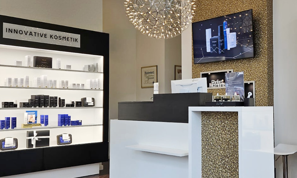Empfang mit Regal „Innovative Kosmetik“, Lichtskulptur und goldener Wand im Institut